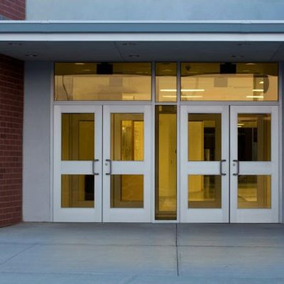 Front entrance of a modern school building with metal and glass doors photographed at at dusk in the Northeastern USA using a Canon 5D MarkII DSLR. Interior is lit up and reflecting a subtle glow onto the concrete ground.